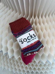 Red and blue patterned socks on a white label with text against a textured beige background